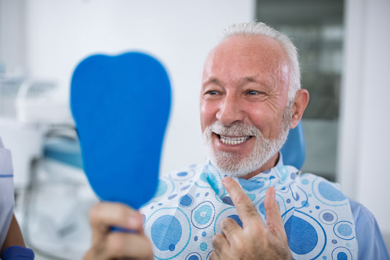 Guy looking in a mirror smiling because he was well tqken care of and has a really nice smile now.